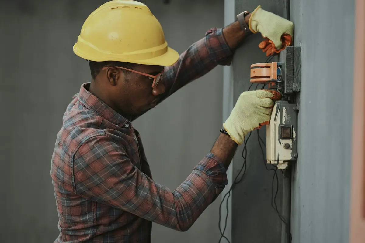 Tradesperson in a hard hat and gloves working on an electrical switchboard