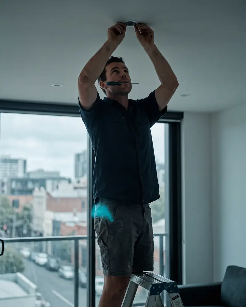 An electrician up a ladder with both hands busy while his phone rings in his pocket